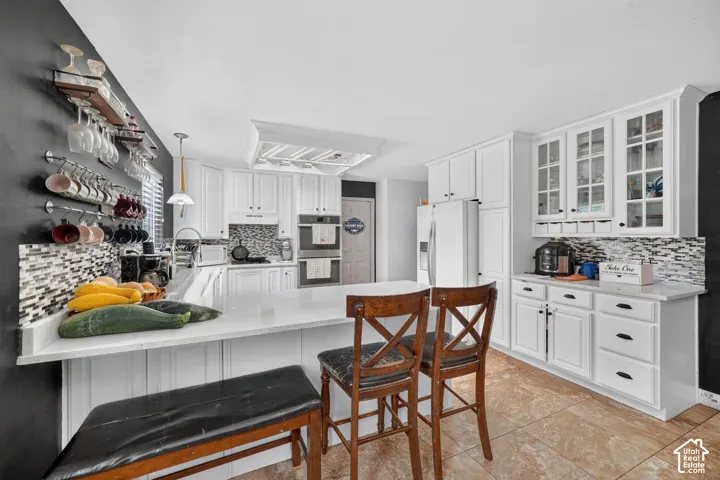 Kitchen featuring white cabinetry, light-toned countertops, a mosaic tile backsplash, and tile flooring