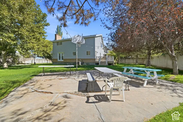 Expansive concrete patio with a spacious grass area, mature trees, and a privacy fence