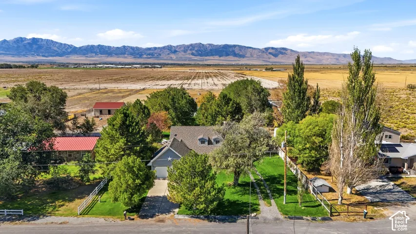 Expansive property featuring a grey siding exterior, attached garage, mature trees, green lawn, and mountain scenery