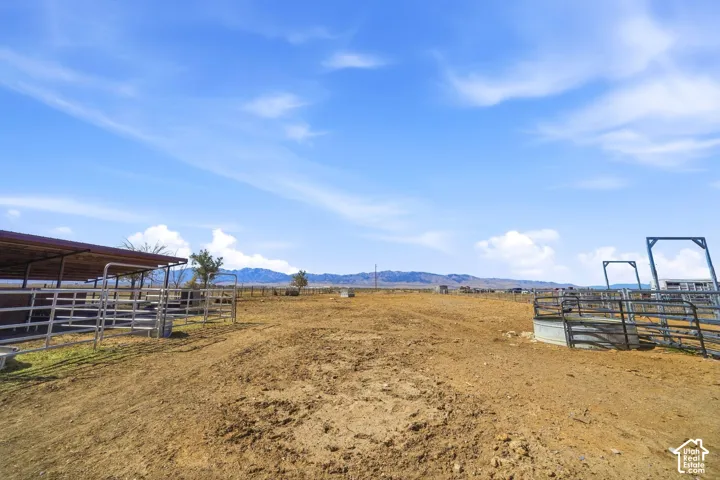 Expansive outdoor area featuring a metal-fenced corral, a covered shelter with a metal roof, and distant mountain scenery