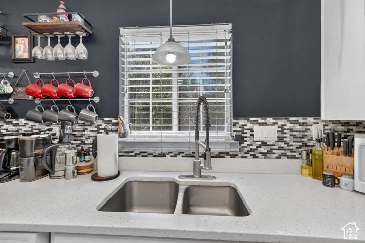 Double basin undermount sink with a flexible neck faucet, complemented by a mosaic tile backsplash, solid surface countertop, and a built-in window with horizontal blinds