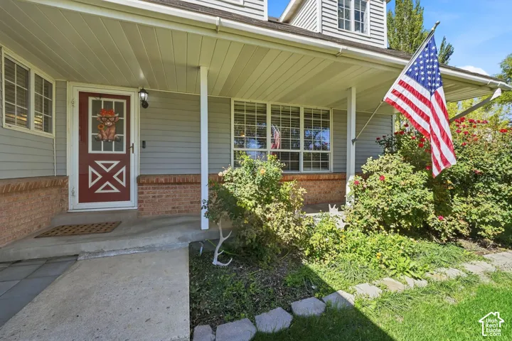 Covered front porch with a red entry door, bay window, and a brick foundation accent
