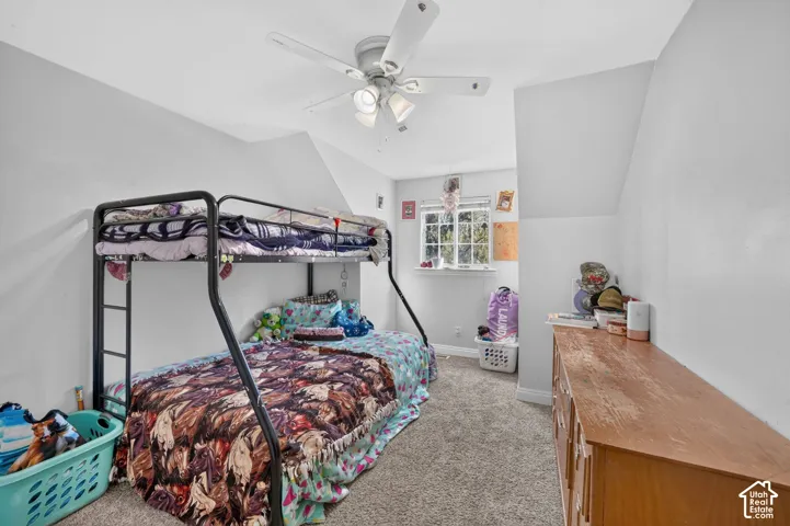 Carpeted room featuring a ceiling fan with integrated lighting, a window with white trim, and sloped ceiling details