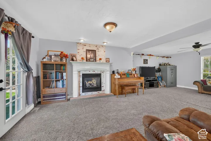 Carpeted living area featuring a central fireplace with a white mantel and brick surround, built-in ceiling light fixtures, and a glass-paned door