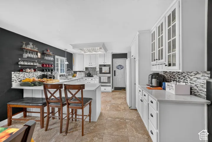 White cabinetry, stone-finish countertops, tile backsplash, built-in double ovens, and tile flooring