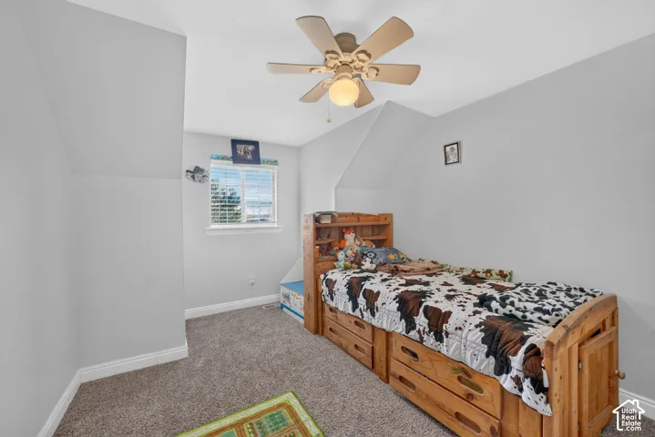 Carpeted flooring, window with blinds, ceiling fan with integrated lighting, and sloped ceiling accents