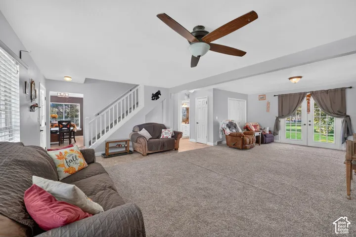 Spacious living area featuring neutral carpeting, a ceiling fan with light fixture, and French doors