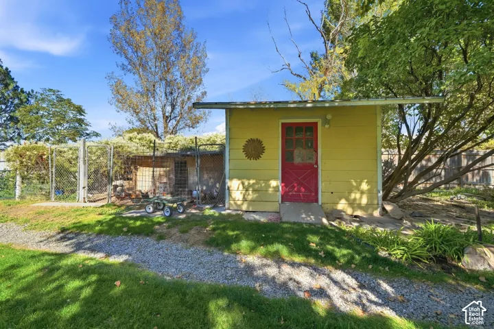 Detached shed with yellow siding and a red paneled door, featuring a gravel path and surrounding green lawn