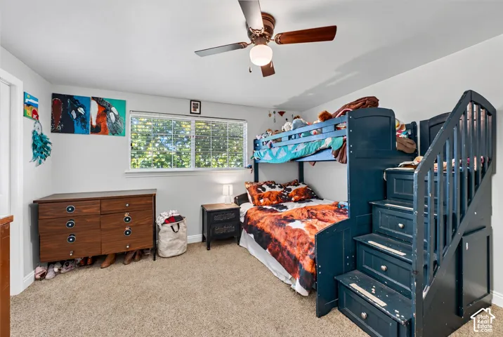 Recessed window with horizontal blinds, overhead ceiling fan with light fixture, light gray wall paint, and neutral tone carpet