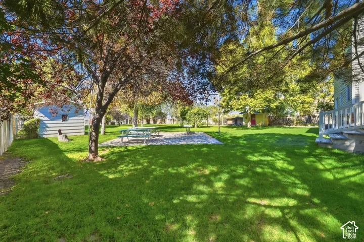 Expansive grassy yard with mature trees providing shade, a paved patio area, and a white wood-sided exterior