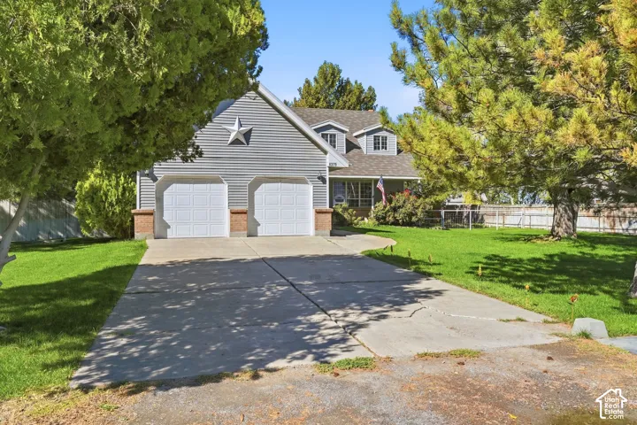 Two-car garage with white panel doors, siding exterior, mature landscaping, and a concrete driveway