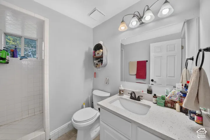 White tile shower with window, white vanity with integrated sink, speckled countertop, and wall-mounted mirror with overhead lighting