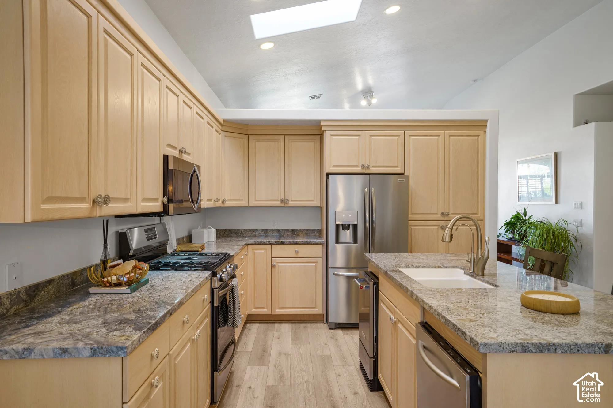 Kitchen featuring light wood cabinetry, stone-finish countertops, stainless steel appliances, and wood-finish flooring