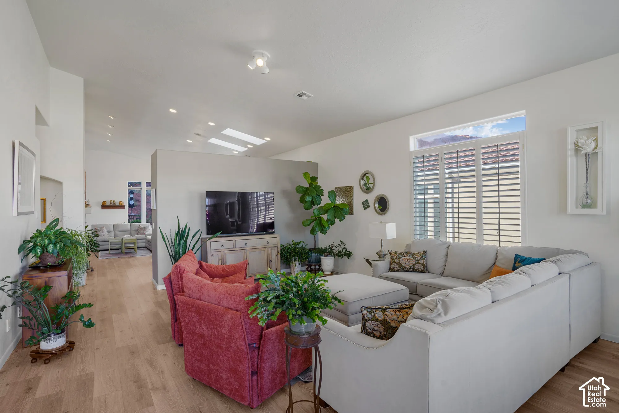 Vaulted ceiling with skylights, recessed lighting, wood-finish flooring, and a large window featuring interior shutters