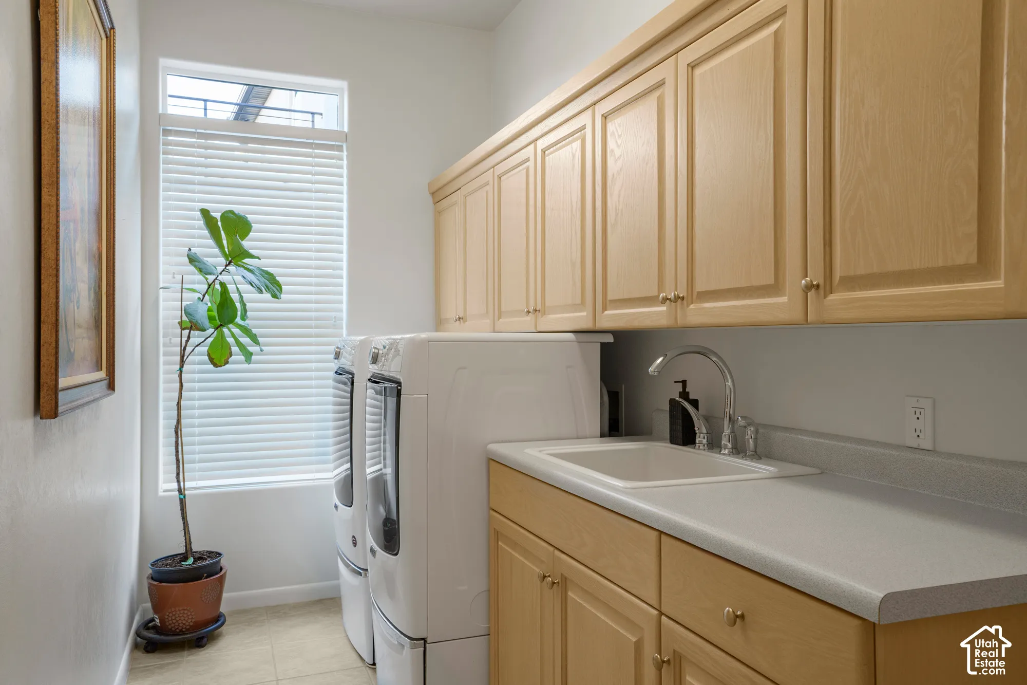 Laundry area with light wood-finish cabinetry, solid surface countertops, and an integrated sink with a chrome faucet