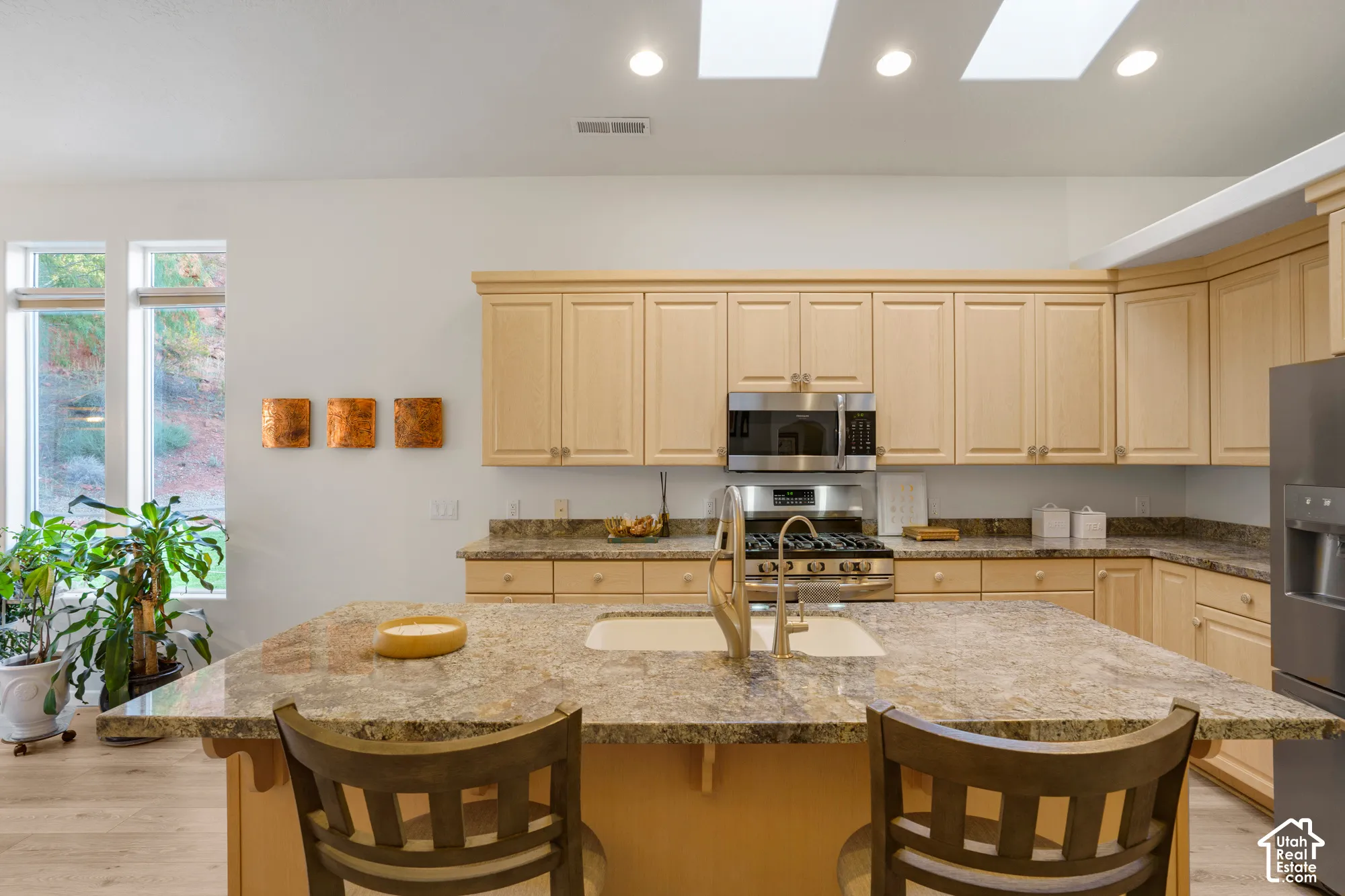 Kitchen featuring an expansive center island with an undermount sink, light wood-finish cabinetry, stainless steel appliances, skylights, and recessed lighting