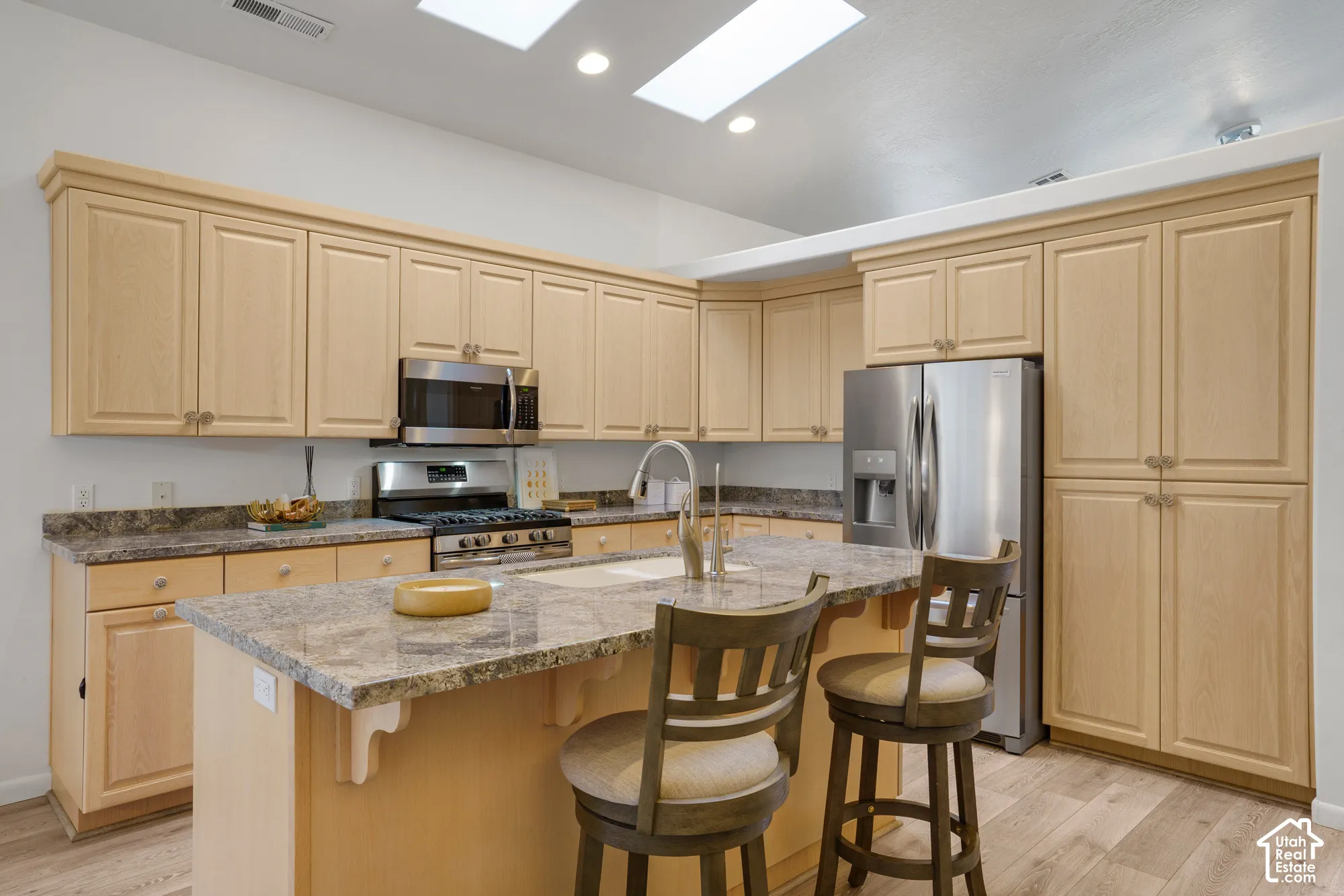 Kitchen featuring light wood cabinetry, stone countertops, stainless steel appliances, and wood-finish flooring
