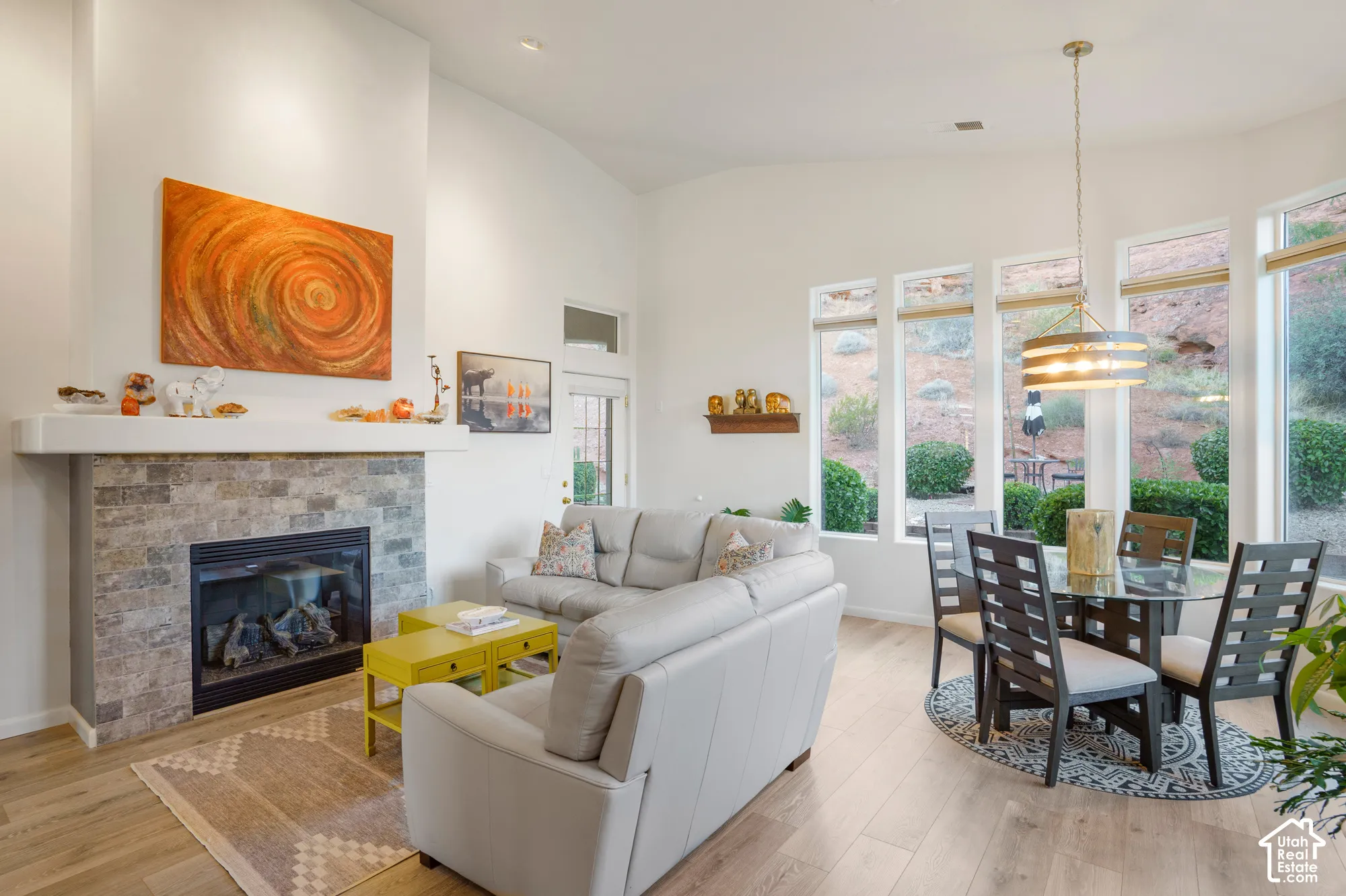 Vaulted ceiling with recessed lighting, stone-front fireplace, wood-finish flooring, and a dining area with a contemporary chandelier