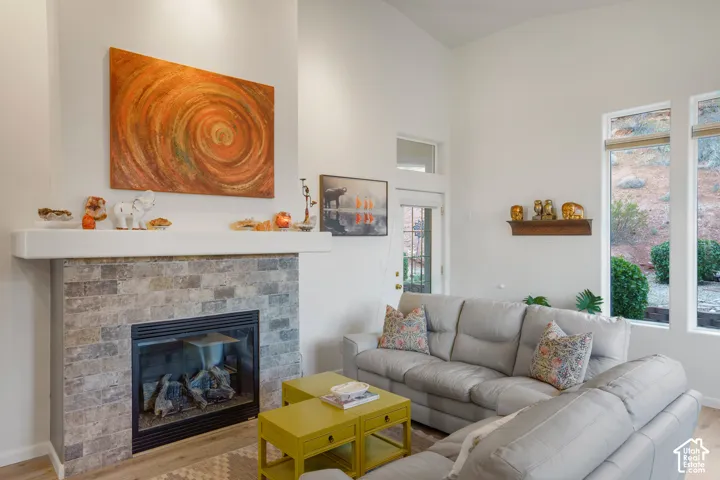 Stone-faced fireplace with a white mantel, vaulted ceilings, and wood-finish flooring