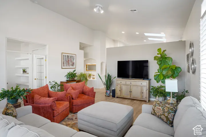 Vaulted ceiling with skylights, wood-finish flooring, built-in shelving, track lighting, and a partial wall feature