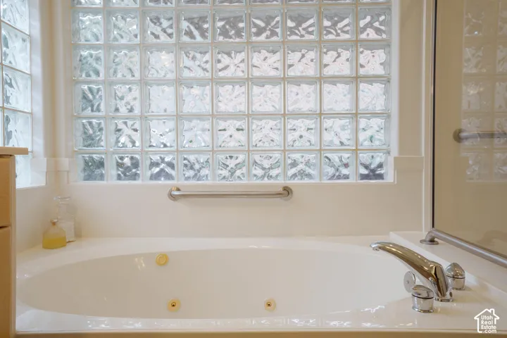 Built-in soaking tub with polished chrome fixtures and grab bars, featuring a glass block privacy window