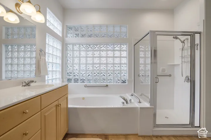 Bathroom featuring a double vanity with light wood cabinetry, a built-in soaking tub, a separate glass-enclosed shower, and decorative glass block windows
