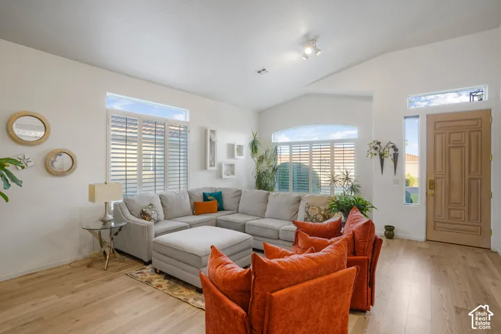 Vaulted ceiling with track lighting, wood-finish flooring, plantation shutters, arched window, and a panel-style entry door