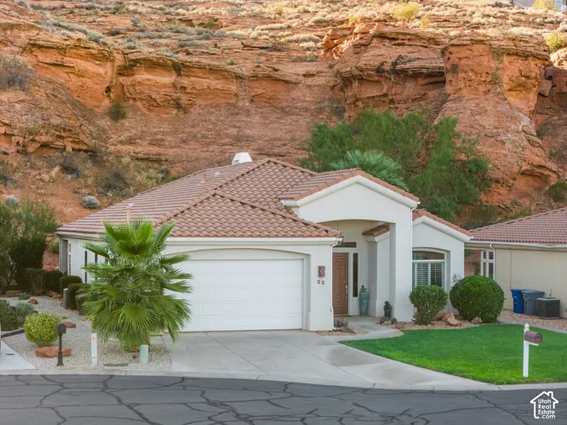 Exterior featuring a tiled roof, attached garage, well-maintained lawn, and established landscaping