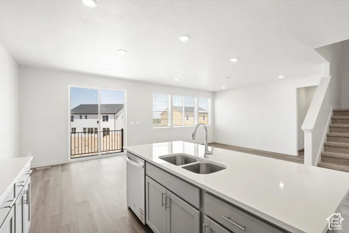 **DICSLAIMER** Interior package may vary.  Kitchen island with a dual basin sink and gooseneck faucet, light wood-finish flooring, recessed lighting, and sliding glass doors to an exterior balcony