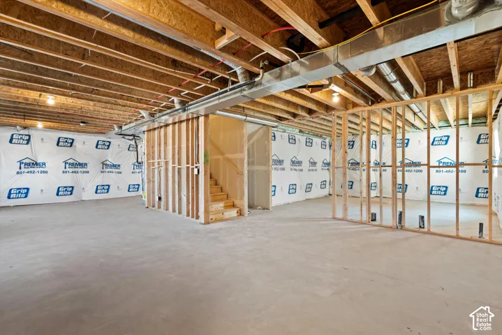 Unfinished basement with concrete flooring, exposed wood joists, and framed walls