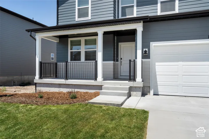 Welcoming covered porch with black railings, concrete steps, and a panel garage door
