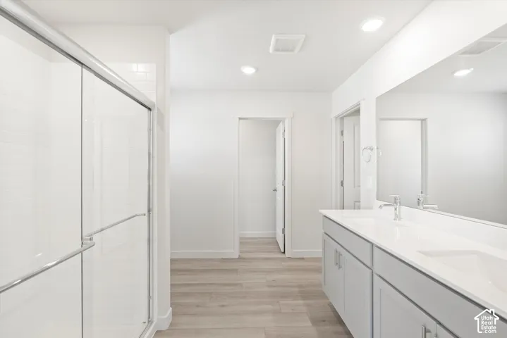 **DICSLAIMER** Interior package may vary.  Dual vanity with integrated sinks, large wall-mounted mirror, glass-enclosed shower, white subway tile shower surround, and wood-finish flooring