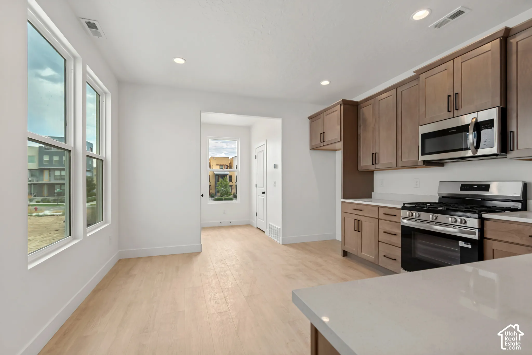 Kitchen and dining area featuring wood-finish flooring, recessed lighting, white walls, wood-finish cabinetry, and stainless steel appliances