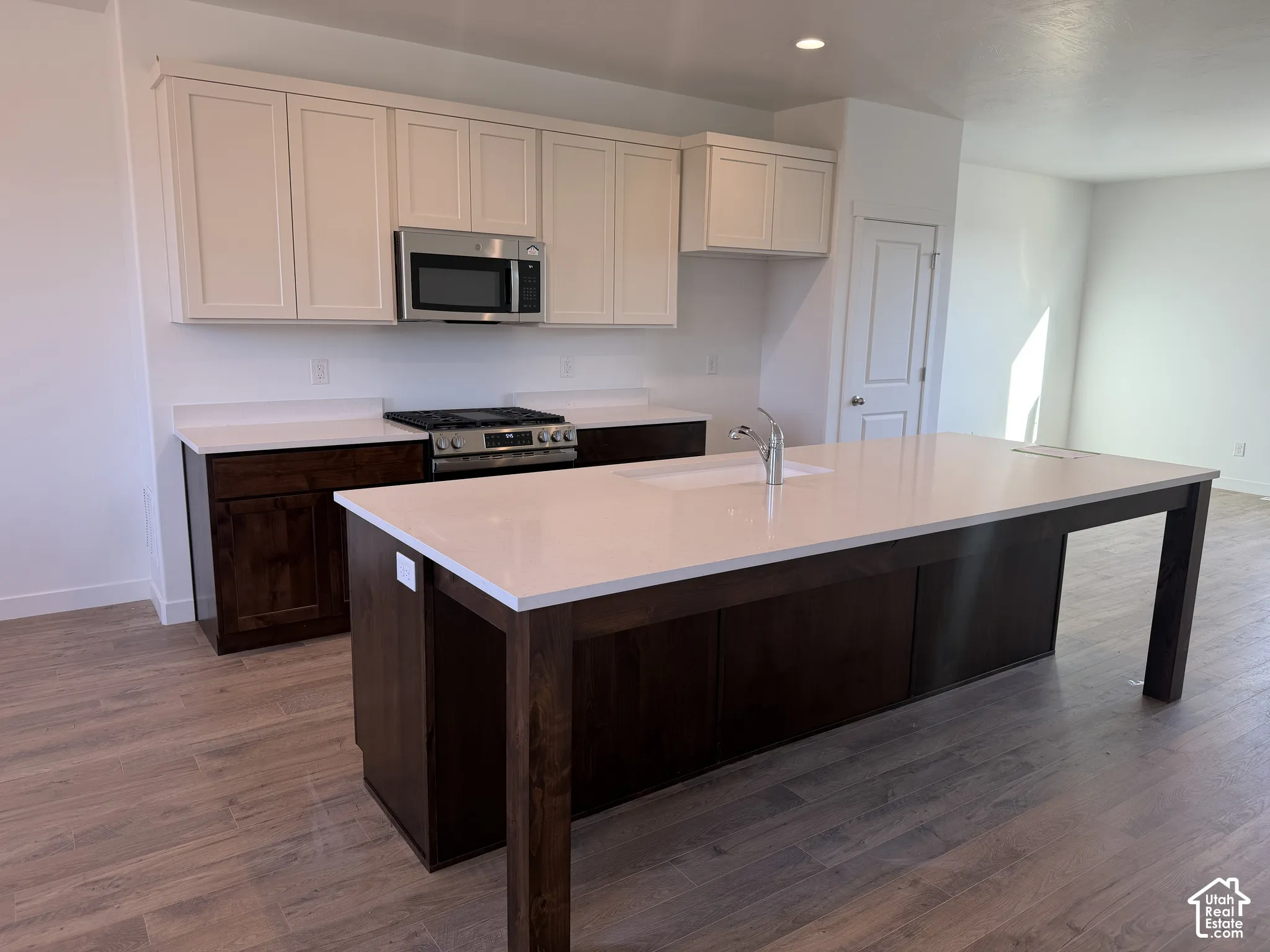 Kitchen featuring wood-finish flooring, two-tone cabinetry, stainless steel appliances, a center island with an integrated sink, and light-toned countertops