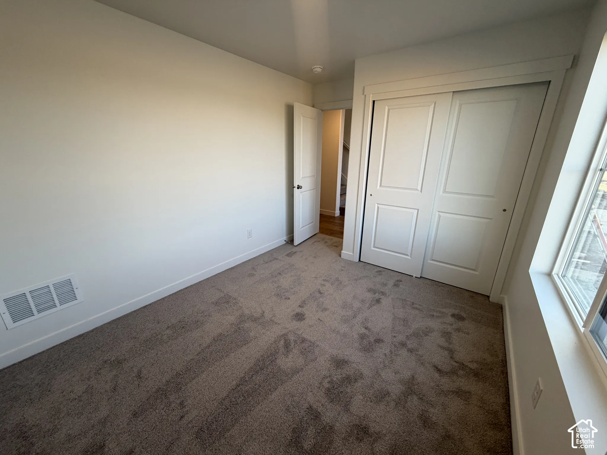 Neutral-toned carpeting paired with white walls, a white sliding closet door, and a white window frame
