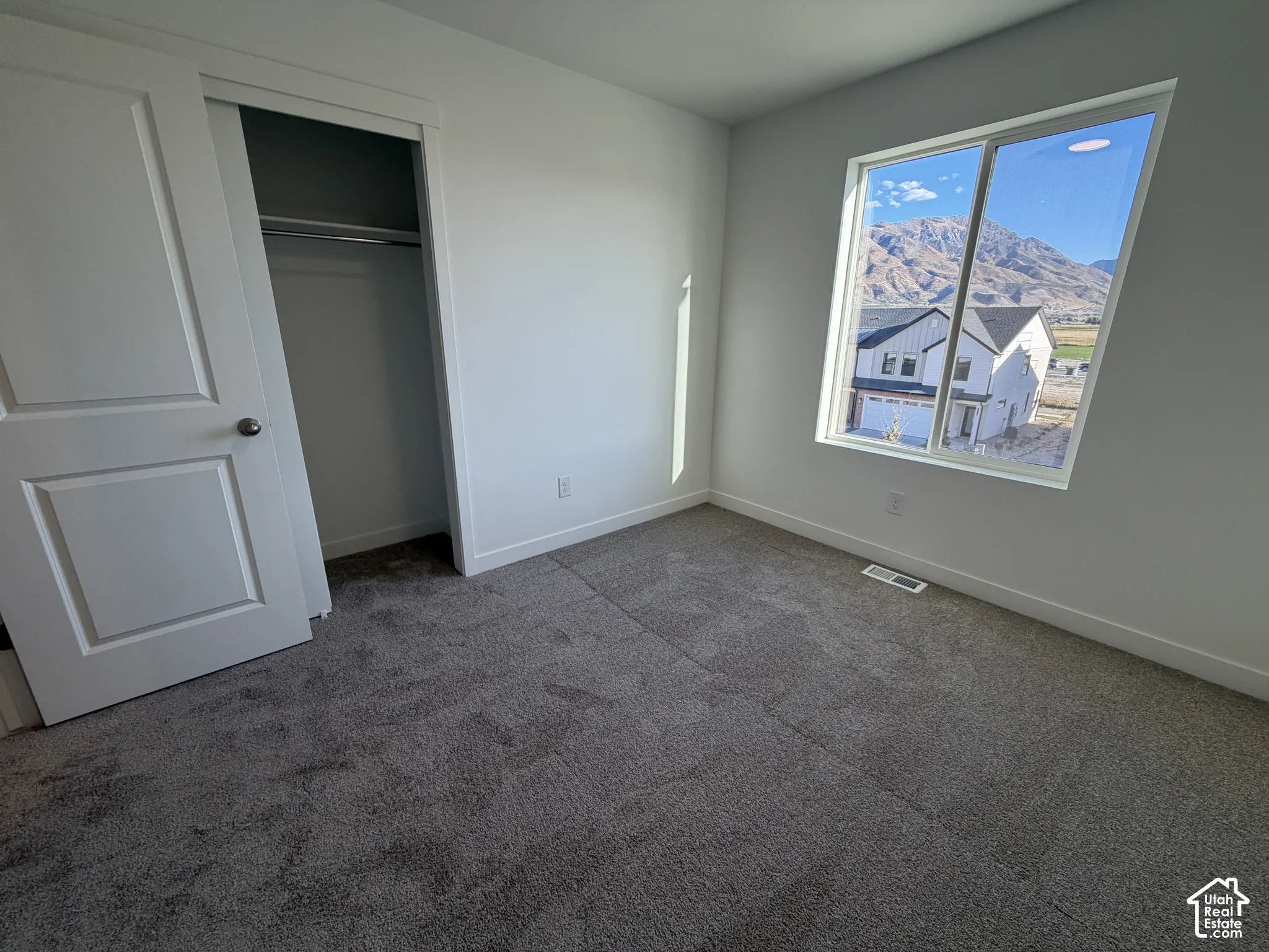 Plush gray carpeting, white painted walls, a built-in closet with a sliding door, and a large window with a mountain backdrop