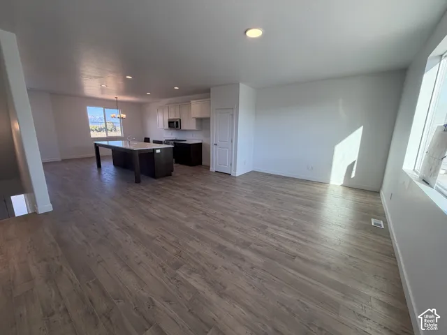Open-concept living area with wood-finish flooring, recessed lighting, a kitchen island with seating, a stainless steel microwave, and white cabinetry