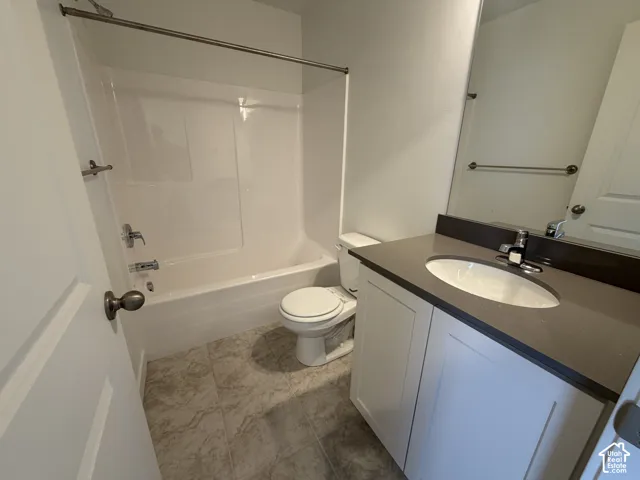 Bathroom featuring a white vanity with a dark countertop, an undermount sink, a toilet, and a combined shower and tub with a white surround