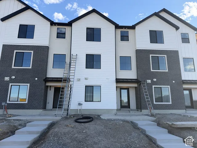 Contemporary townhome exterior featuring multi-level construction, white horizontal siding, dark brick accents, and black-framed windows