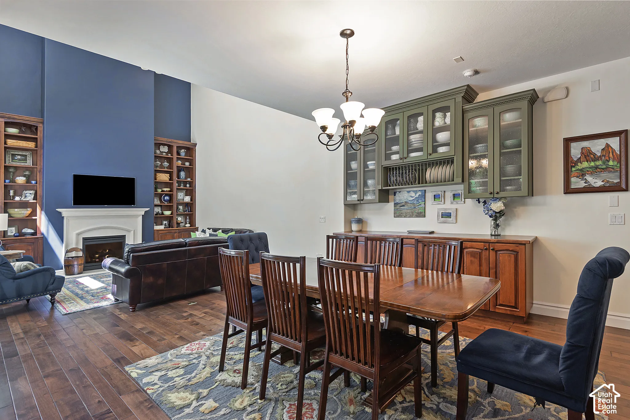 Hardwood flooring throughout, featuring a fireplace with a stone mantel, built-in shelving, an elegant chandelier, and custom display cabinetry