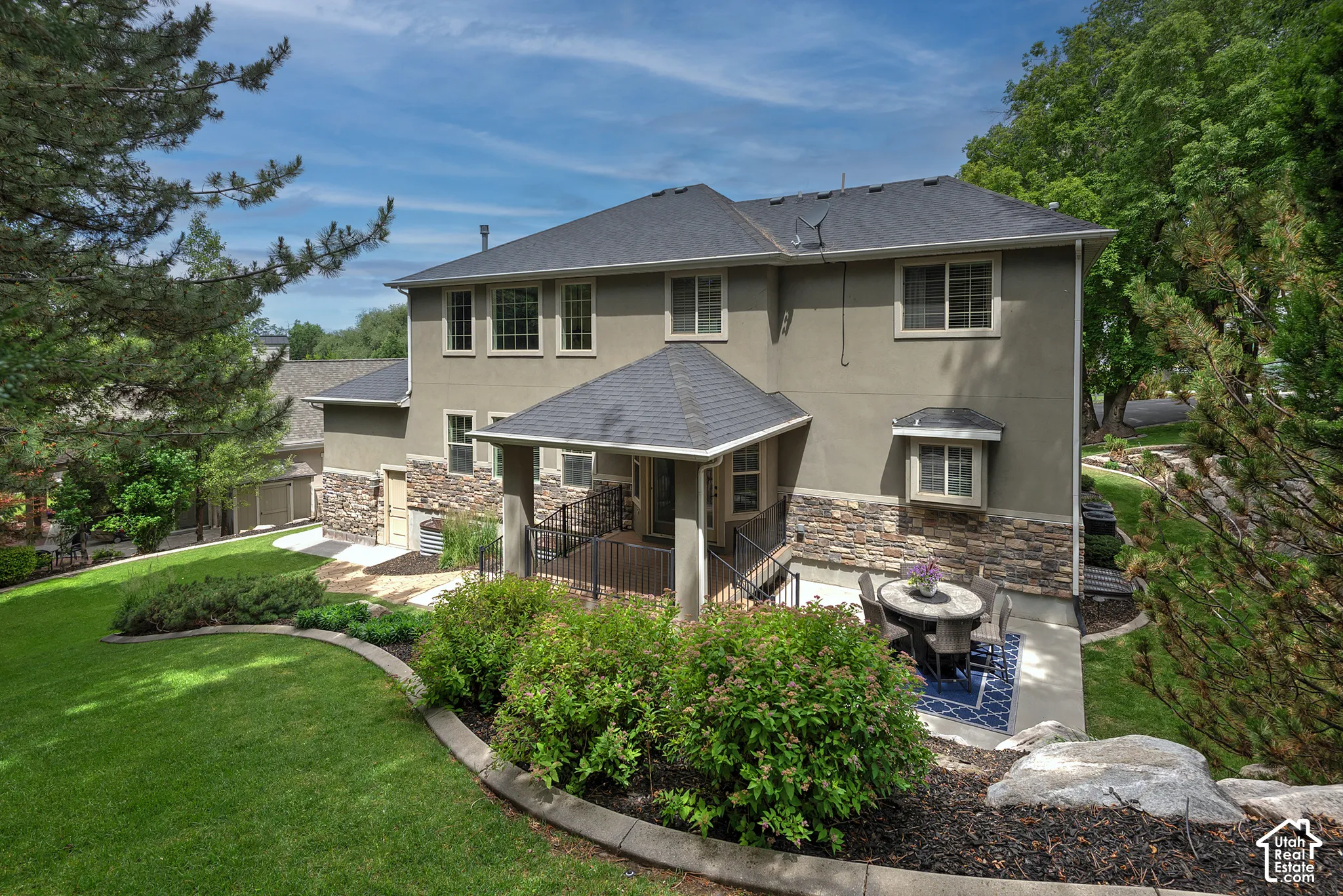 Expansive backyard featuring a manicured lawn, layered landscaping, a lower-level patio, and a covered entry