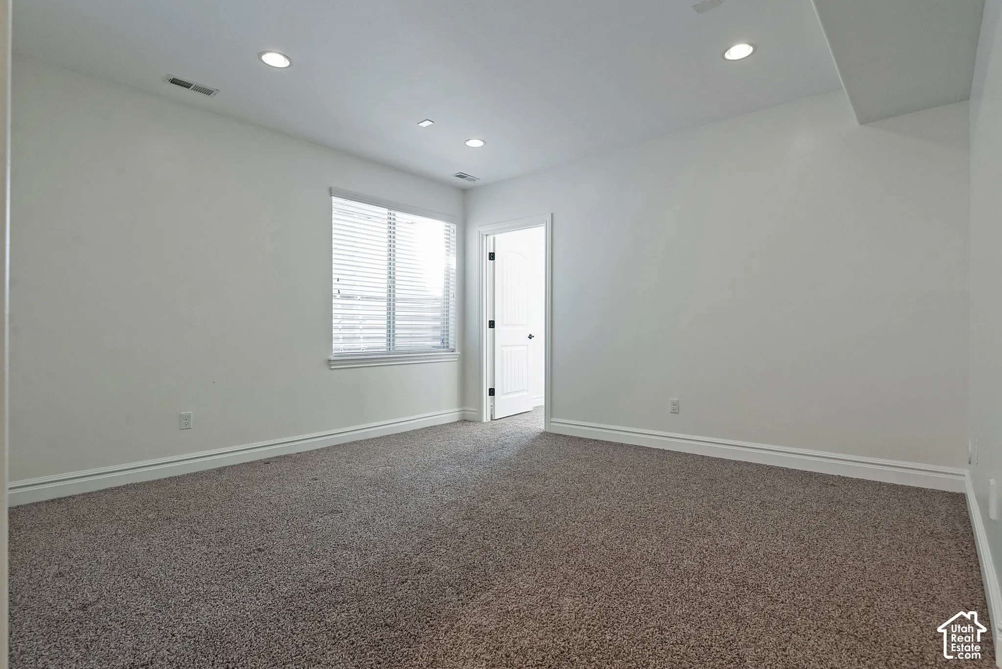 Bright, open bedroom featuring neutral wall finishes, recessed ceiling lighting, carpeted flooring, and a window with plantation shutters