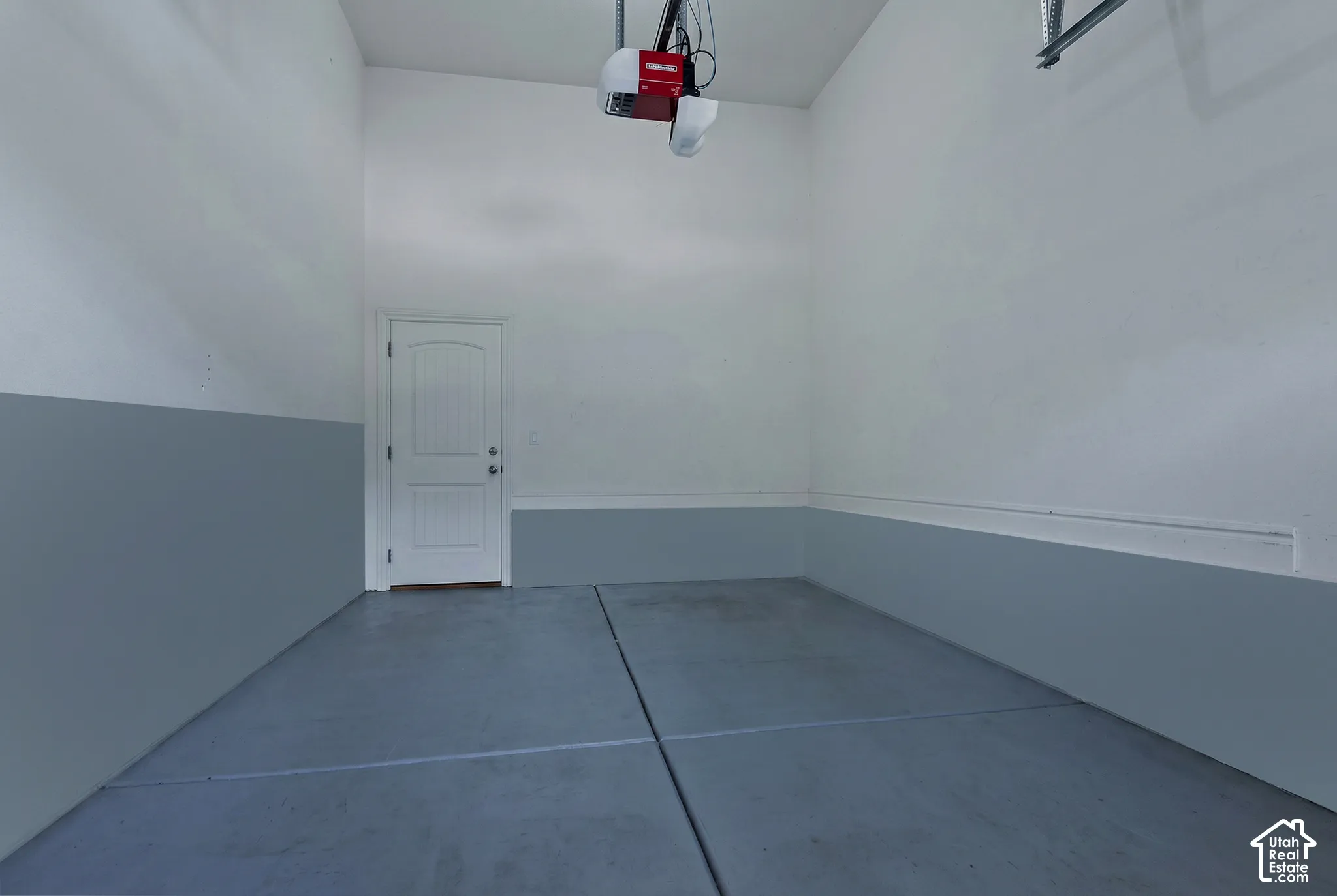 Attached garage with a finished concrete floor, painted interior walls, overhead garage door opener, and a panel door