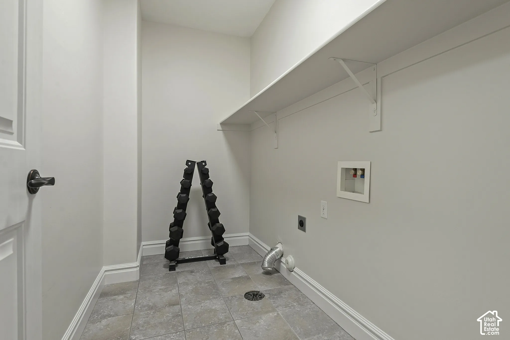 Tiled flooring with a central floor drain, a wall-mounted utility sink connection, and an integrated shelf with support brackets