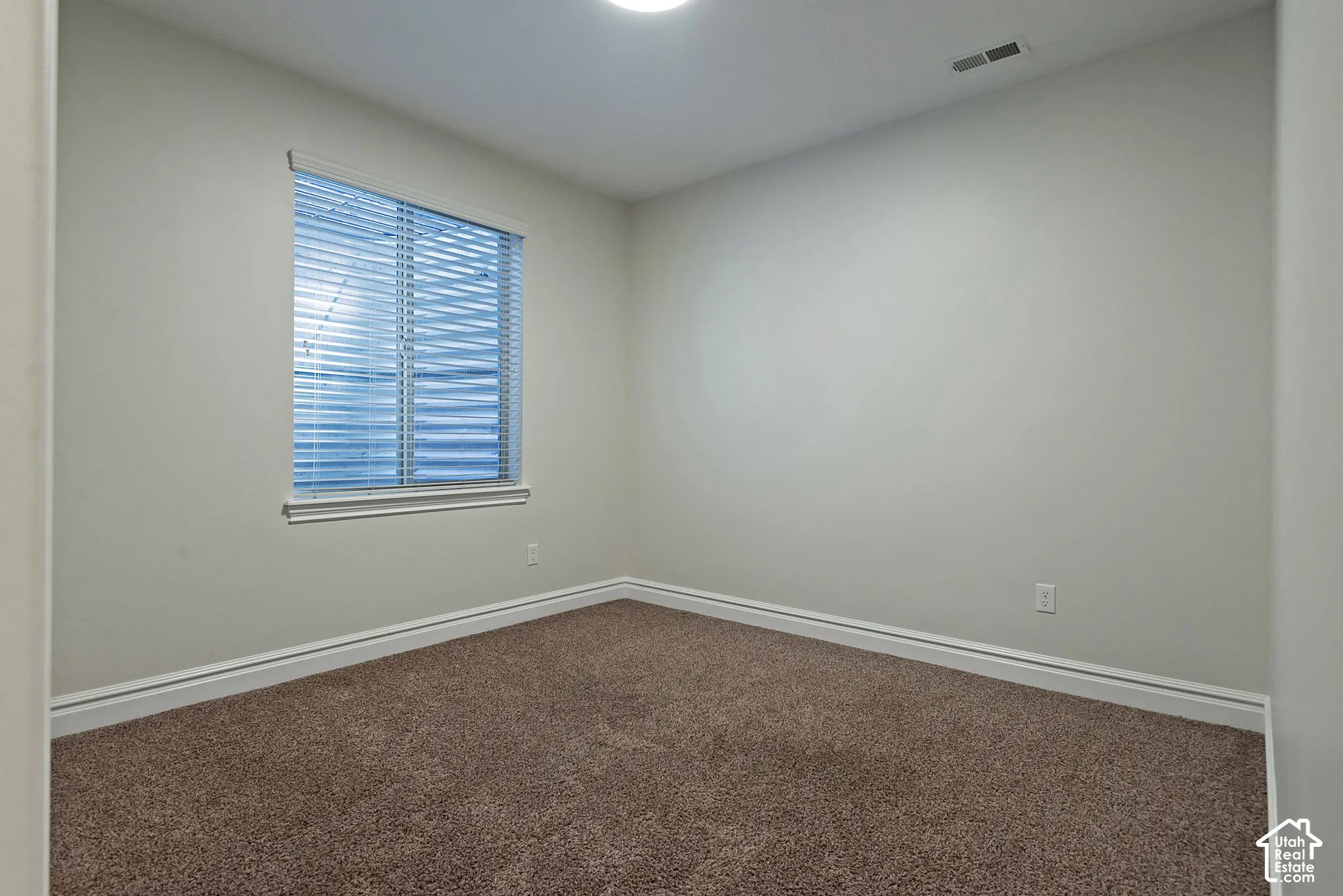Bright corner bedroom featuring neutral wall finishes, abundant natural light from a large window with plantation shutters, and plush carpeting throughout