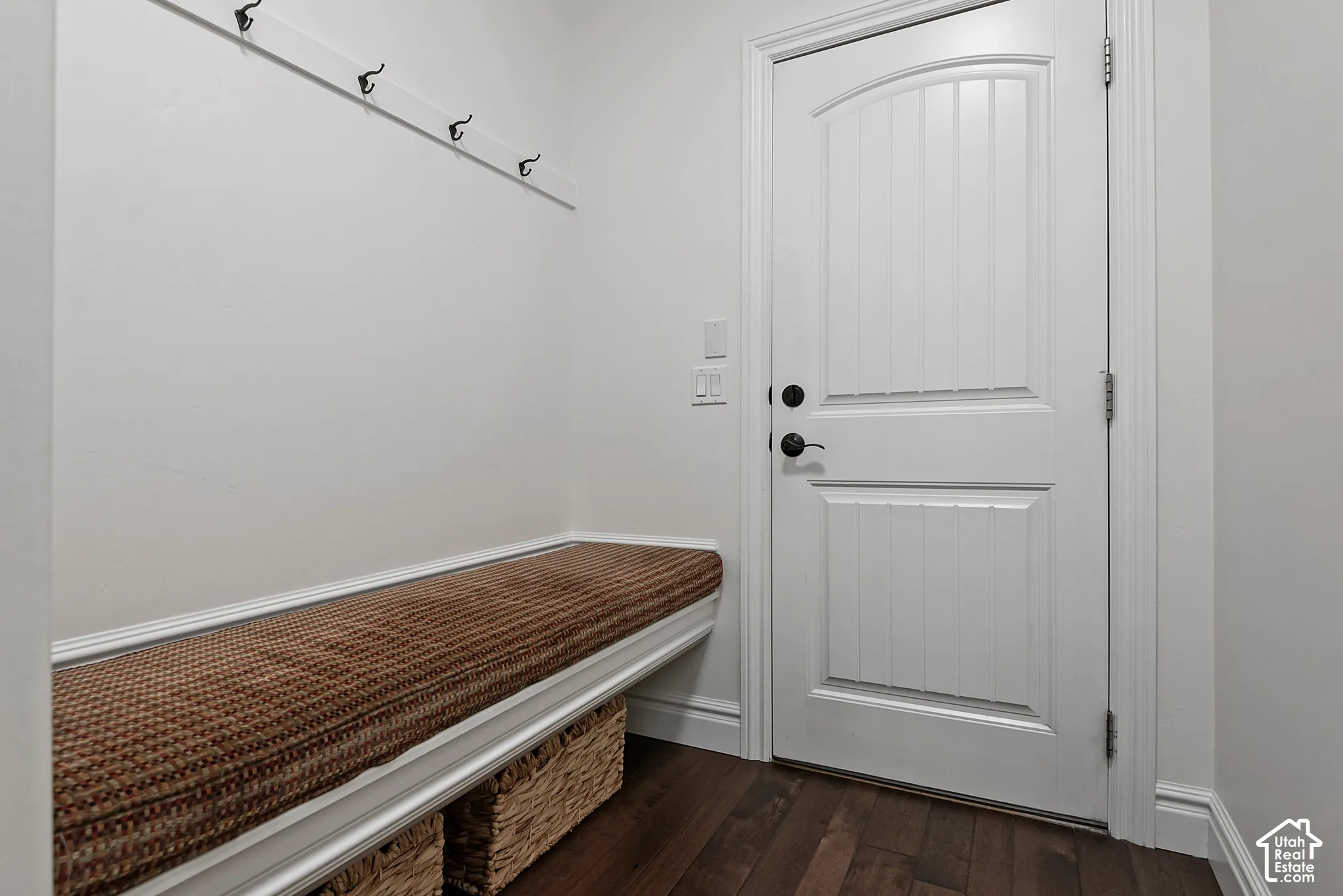 Built-in bench seating with a cushioned top, wall-mounted coat hooks, and wood-finish flooring