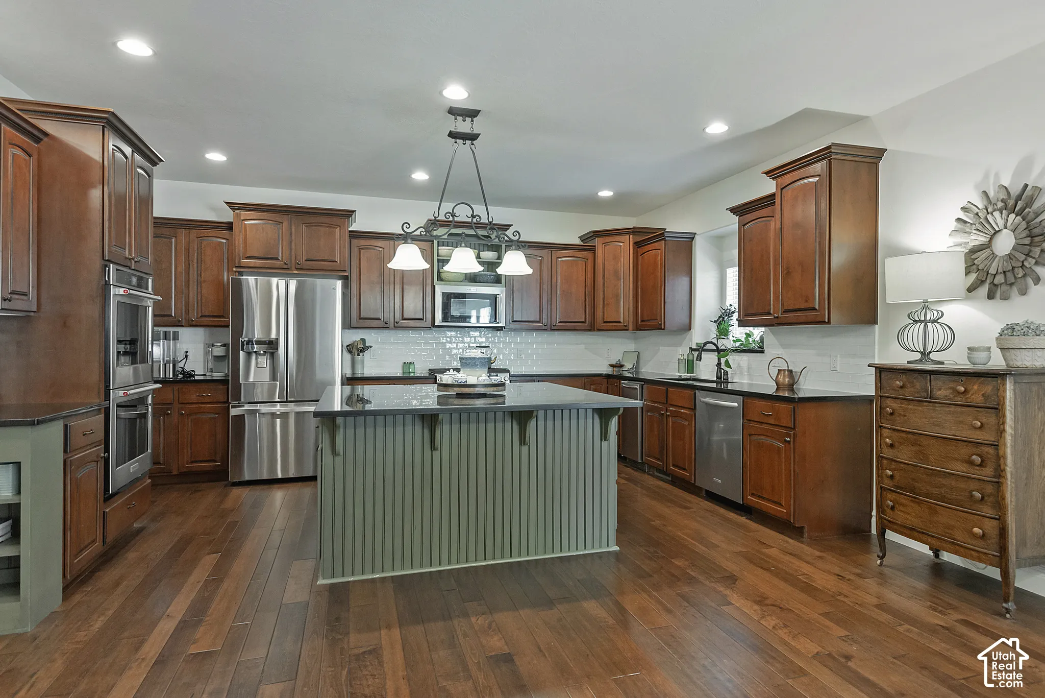 Expansive kitchen featuring wood-finish flooring, dark wood cabinetry, a center island with beadboard trim, stainless steel appliances, and recessed lighting