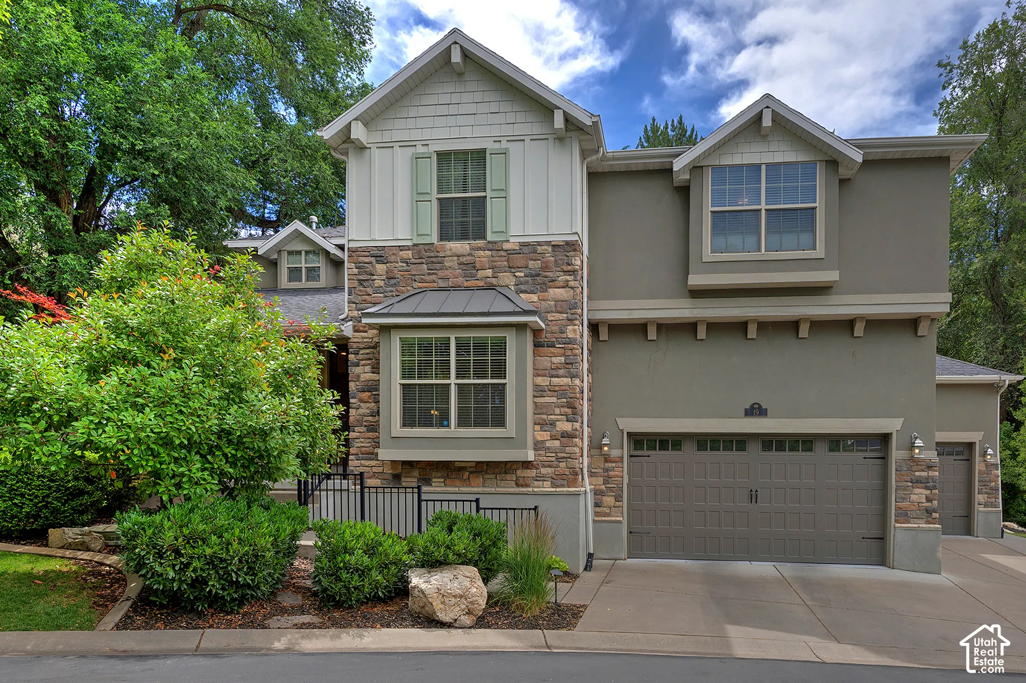 Striking two-story residence featuring a mixed-material exterior of stone and fiber cement siding, complemented by a two-car garage with paneled doors