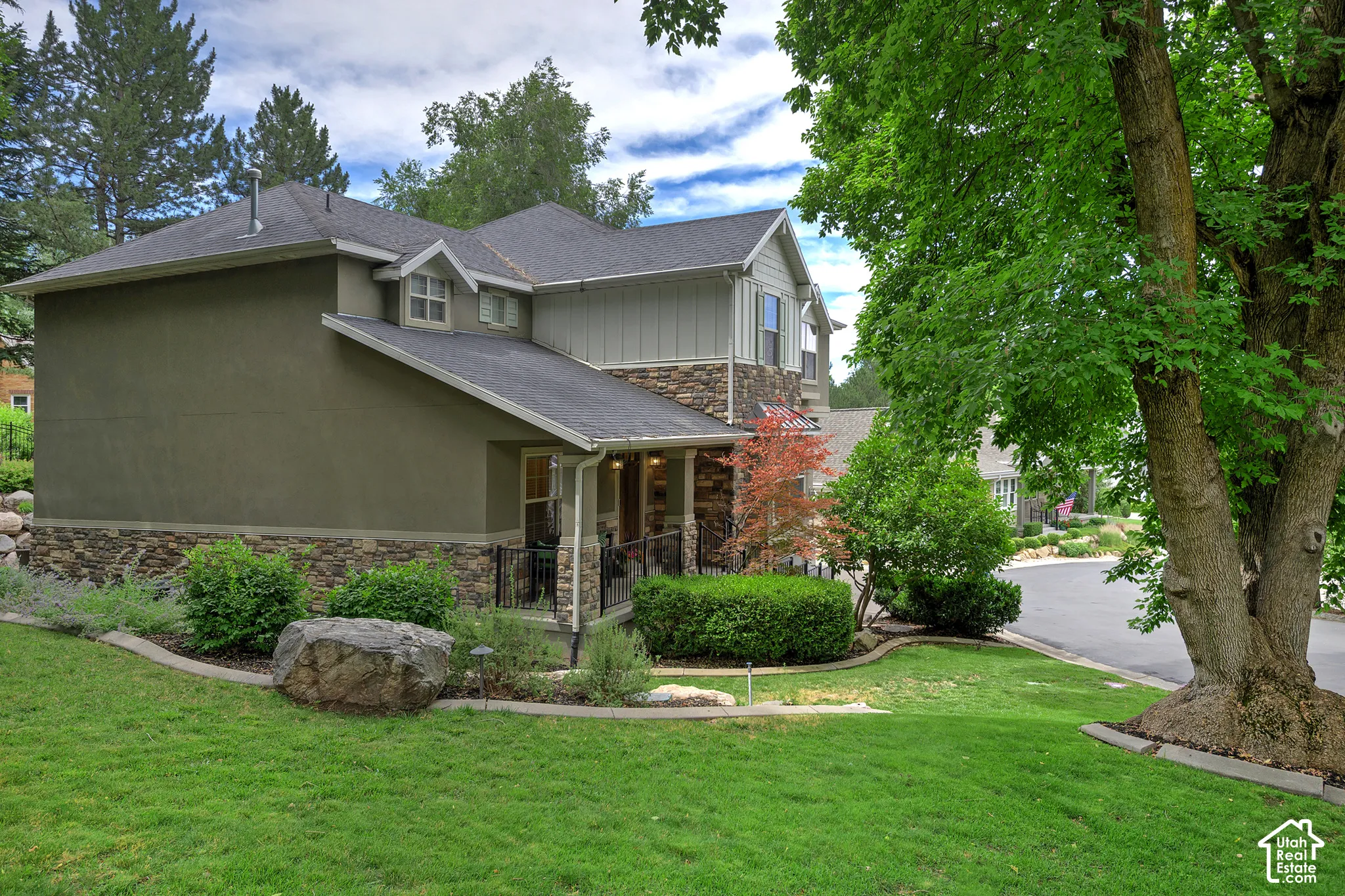 Two-story residence featuring a combination of stucco and stone veneer siding, covered porch entrance with columns, and a dormer window