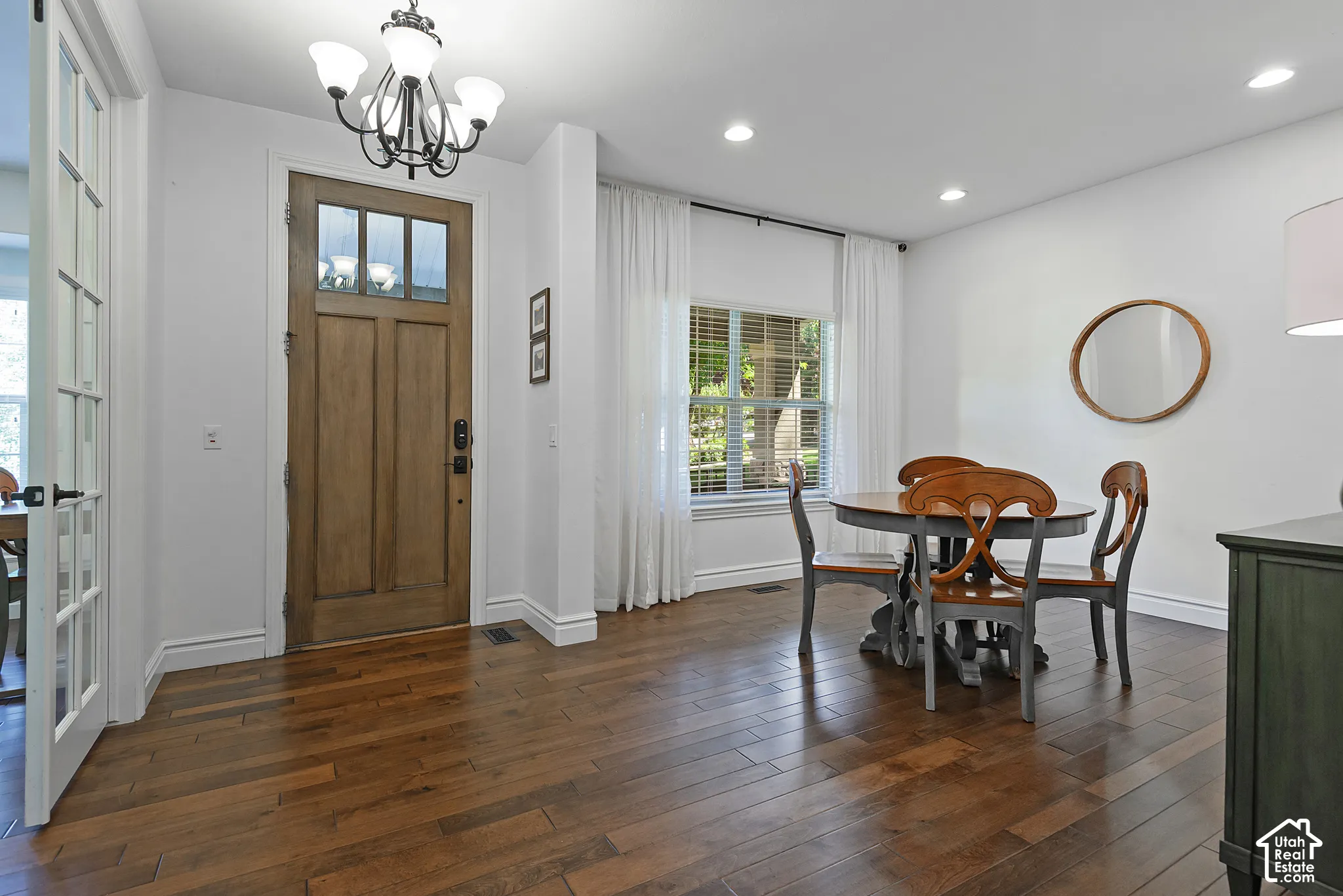 Wood-finish flooring throughout, solid wood front door with glass panels, elegant chandelier, recessed lighting, and a window with white drapes
